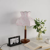 Pink blossom shade lamp unlit beside a flip clock and a book