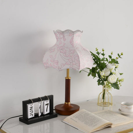 Pink blossom shade lamp unlit beside a flip clock and a book