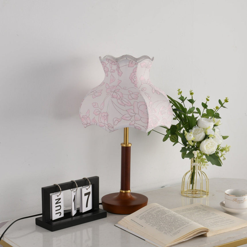 Pink blossom shade lamp unlit beside a flip clock and a book