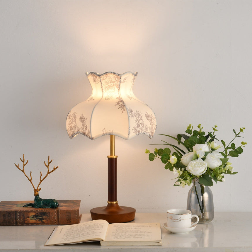 Blossom shade lamp lit on a desk beside an open book and white roses