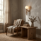 Sconce lit above a bench with a throw beside a wood table and a vase