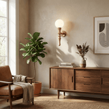 Sconce lit beside a plant above a sideboard with framed art and a window