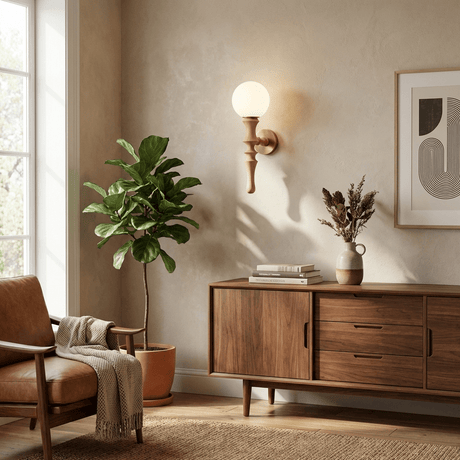 Sconce lit beside a plant above a sideboard with framed art and a window