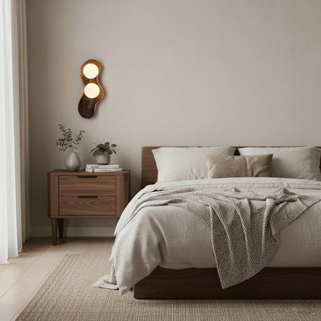 Sconce lit beside a bed above a wood nightstand with a folded throw