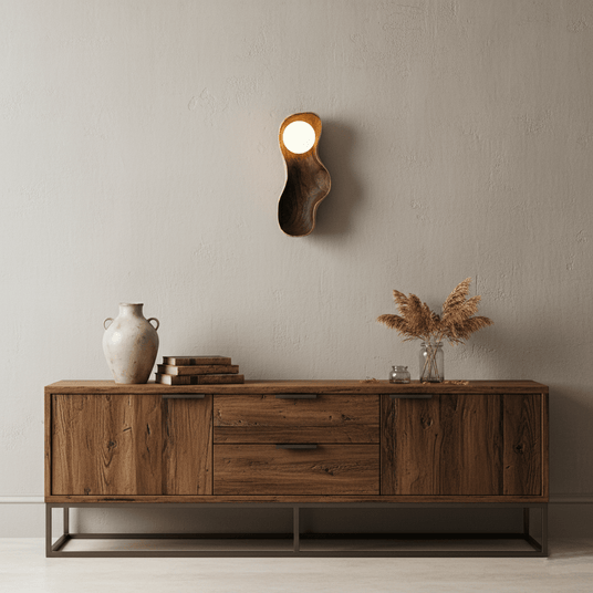 Sconce lit above a wood sideboard holding pale vases and dried stems
