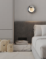 The orbit light lit above a bed with a gray headboard and a marble nightstand