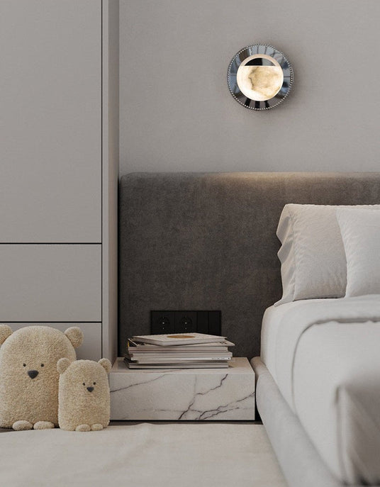 The orbit light lit above a bed with a gray headboard and a marble nightstand