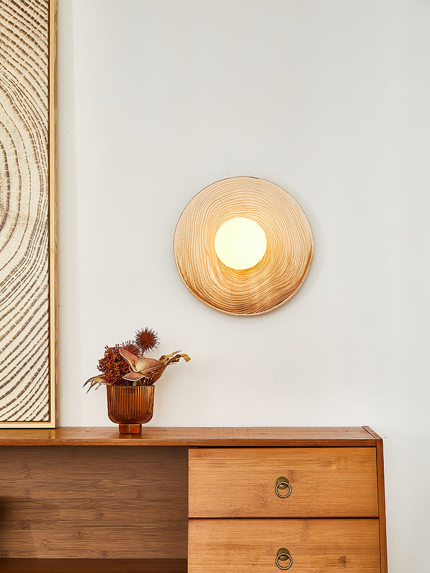 The sconce lit above a chest of drawers beside a framed print