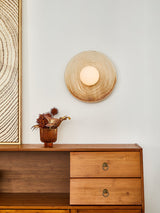 The sconce above a wood dresser with a vase, next to a framed print