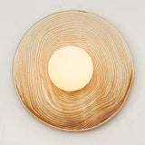 The ringed sconce lit on a pale wall, seen from the front