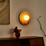 The sconce lit amber above a dark wood sideboard beside a framed print and a bare branch