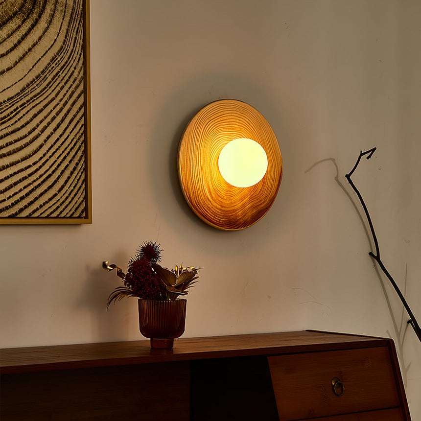 The sconce lit amber above a dark wood sideboard beside a framed print and a bare branch