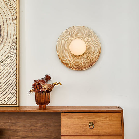 The ringed ceramic sconce above a teak sideboard with drawers and a vase of dried flowers