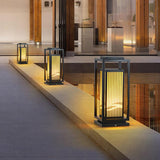 The lantern glowing beside a doorway on a paved terrace in the evening