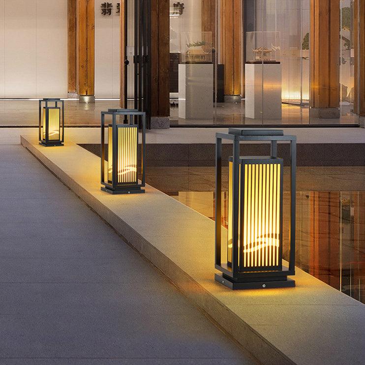 The lantern glowing beside a doorway on a paved terrace in the evening