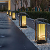 Two cage lanterns lit along a paved path beside low garden planters