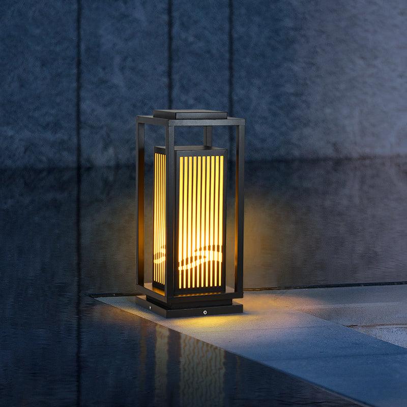The lantern lit on paving beside still water with planting behind