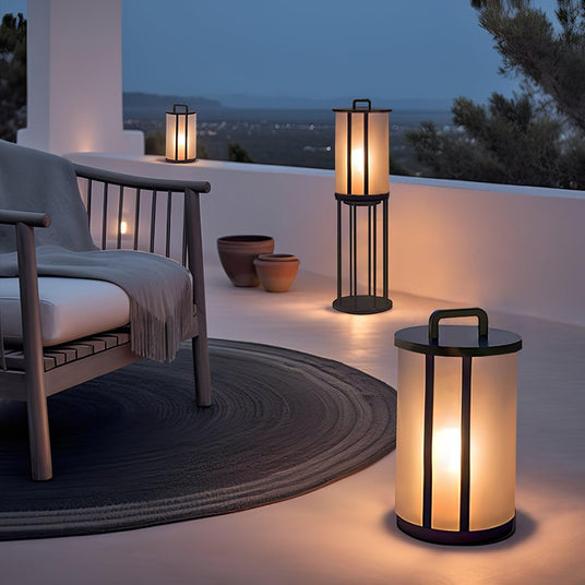 Lanterns lit on a white terrace above the sea beside a low chair at dusk
