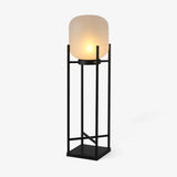 Opal cylinder shade resting in an open square steel stand in black