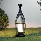 The cage lantern lit on a lawn against a pale evening sky