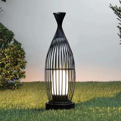 The cage lantern lit on a lawn against a pale evening sky