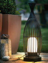 The lantern lit beside tall planters and pale stones on a terrace
