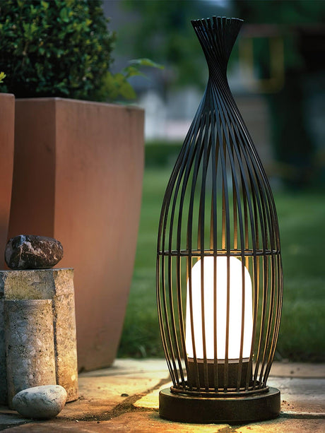 The lantern lit beside tall planters and pale stones on a terrace