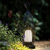 The lit inner cylinder seen through the cage among garden planting