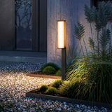 One arm lit at a gravel edge beside grasses and a lit house wall