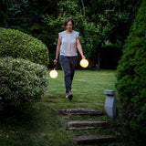 Two lamps carried by their ring handles across a lawn at dusk