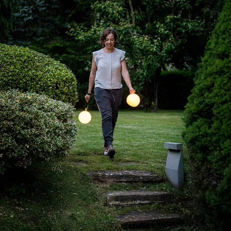 Two lamps carried by their ring handles across a lawn at dusk