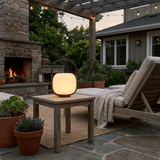 The lamp lit on a side table beside an outdoor fireplace and a lounger