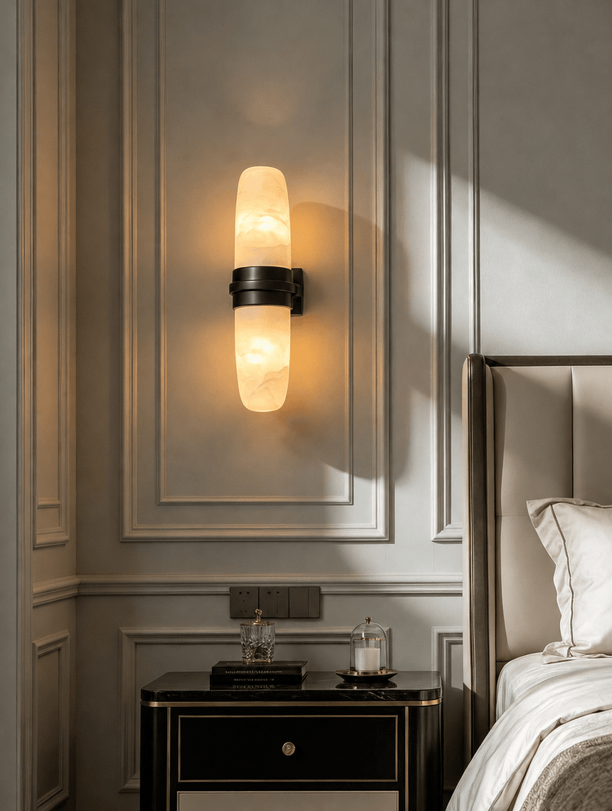 The sconce lit on a paneled wall beside a bed and a mirrored nightstand