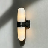 The black bracket and lit tube seen at an angle on a pale wall