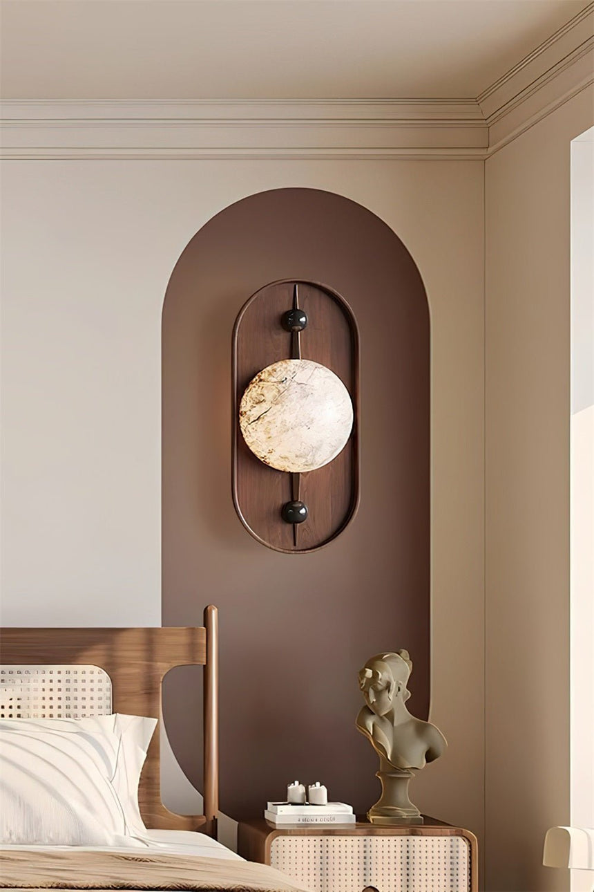 Sconce lit on an arch panel above a bed piled with pale cushions