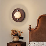 Sconce lit beside a bed with a curved wood headboard and dried flowers