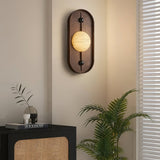 Sconce lit above a black sideboard with a vase of branches and a palm
