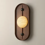 The tall walnut pill seen from the front, the veined disc lit across its middle