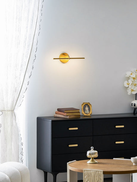 Lit beside a long curtain above a dark dresser with books and a small vase