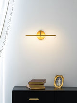 The gold rod lit above a black sideboard holding books and a framed portrait