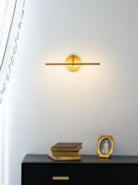 The gold rod lit above a black sideboard holding books and a framed portrait