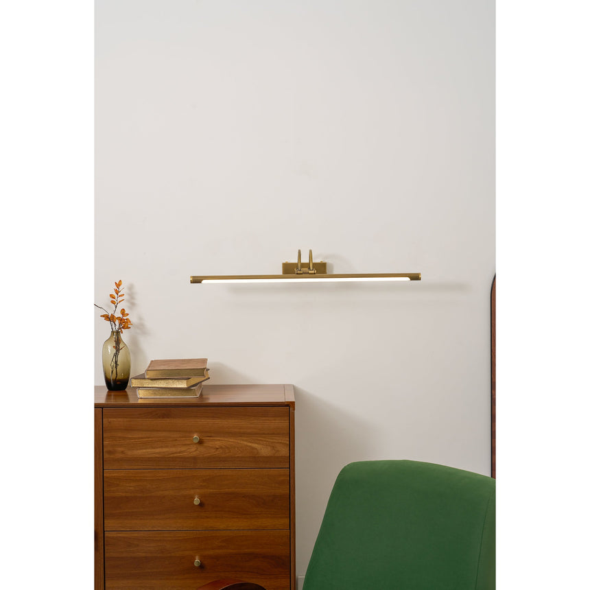 Brass bar lit above a walnut chest of drawers beside a green upholstered chair