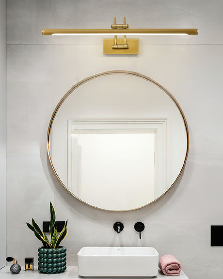 Brass bar over a round mirror on a concrete wall above a white basin and plants