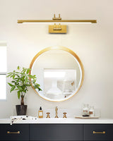 Long brass bar lit over a round mirror above a navy vanity with bottles and a plant