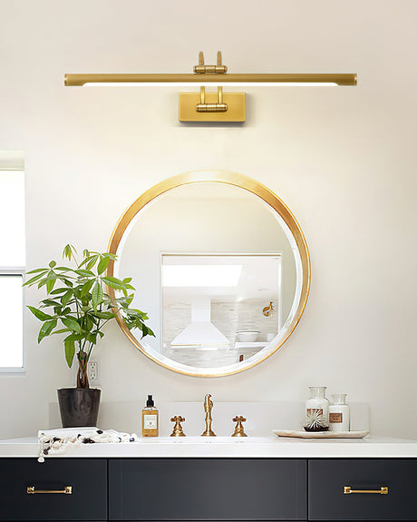 Long brass bar lit over a round mirror above a navy vanity with bottles and a plant