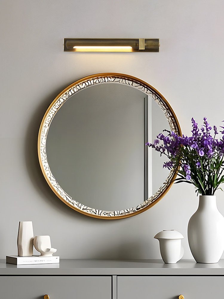 Bronze bar lit above a round beaded mirror over a gray chest of drawers