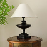 Black oversized table lamp seen from the side on a round wooden table