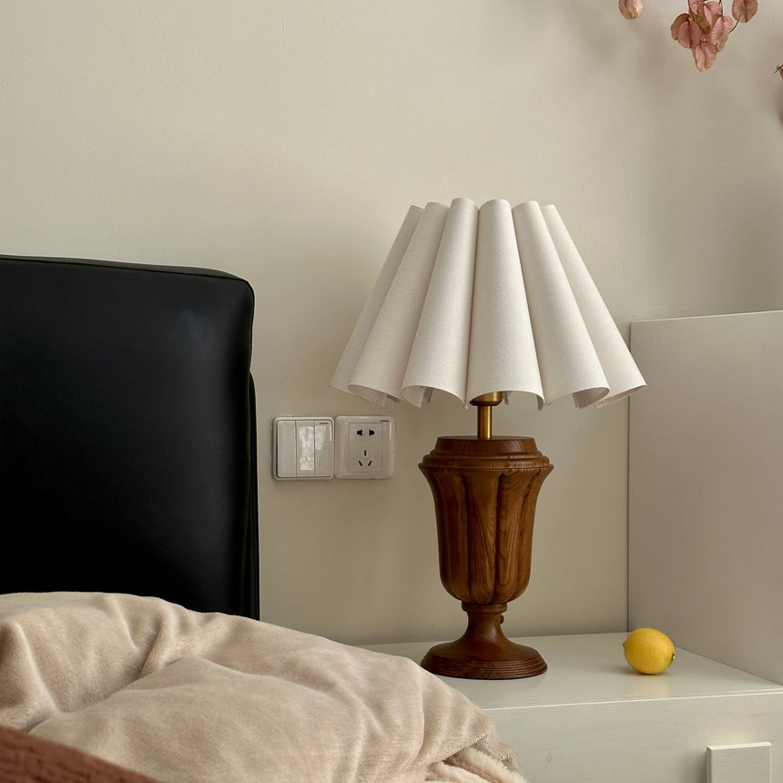 Urn base lamp lit on a nightstand beside a dark leather headboard