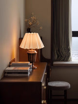 Urn base lamp lit on a desk beside a window and dark curtains