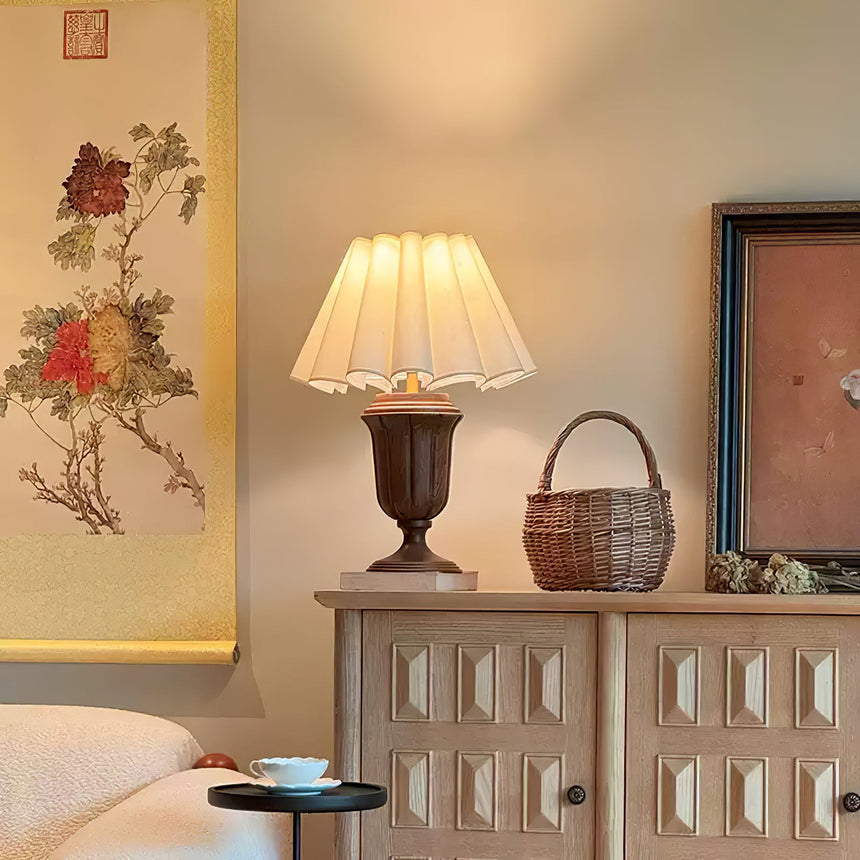 Urn base lamp lit on a cabinet beside a bed and a hanging scroll